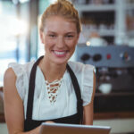 Kvindelig cafémedarbejder står og smiler med Nem Booking bordbookingsystem på tablet
