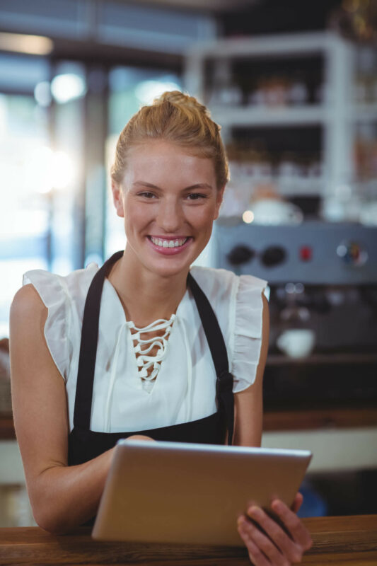 Kvindelig cafémedarbejder står og smiler med Nem Booking bordbookingsystem på tablet